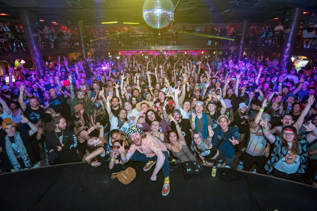 A packed venue photographed from the stage, hands in the air.